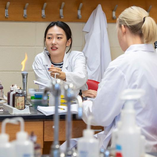 两个穿着白大褂的女学生在科学实验室工作.